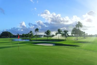 Golf green with red flag by a sand bunker and pond beneath sprinkler spray in Miami Lakes Golf Club at Miami Lakes Hotel