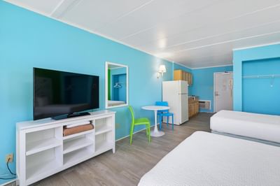 HC Ground Floor Poolview Efficiency with two beds facing TV, wall mirror & kitchenette & dining area at Kokomo Suites