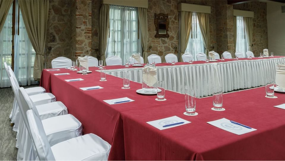 Gran mesa en U en Salón Virreinal con manteles rojos y muros de piedra en Quinta Real Guadalajara