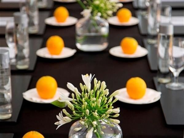 Elegant table setting at El Prado Hotel with a black cloth, fresh oranges, and white floral centerpieces
