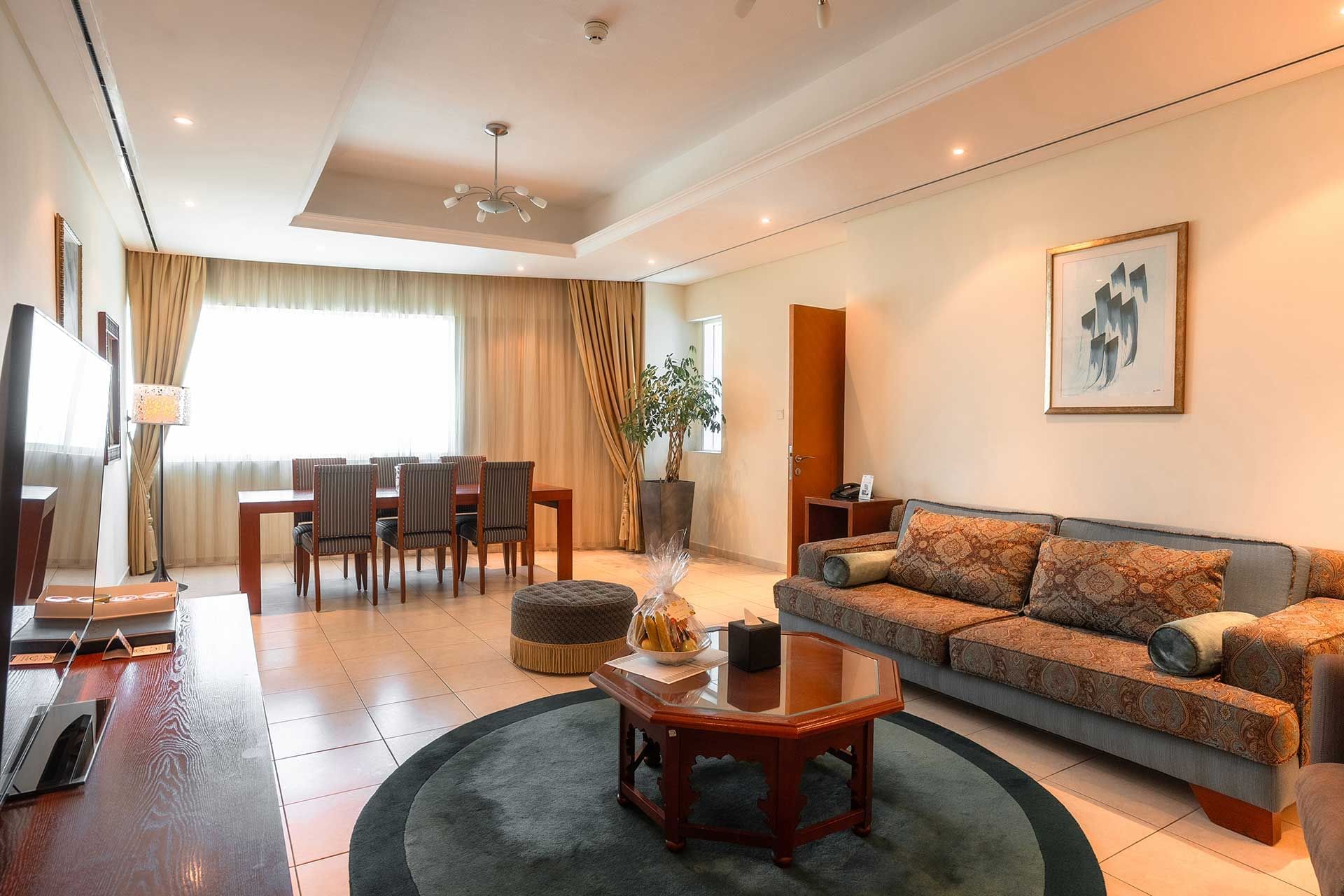 TV lounge with wooden dining table by the window and tiled floors in room at Tamani Marina Hotel