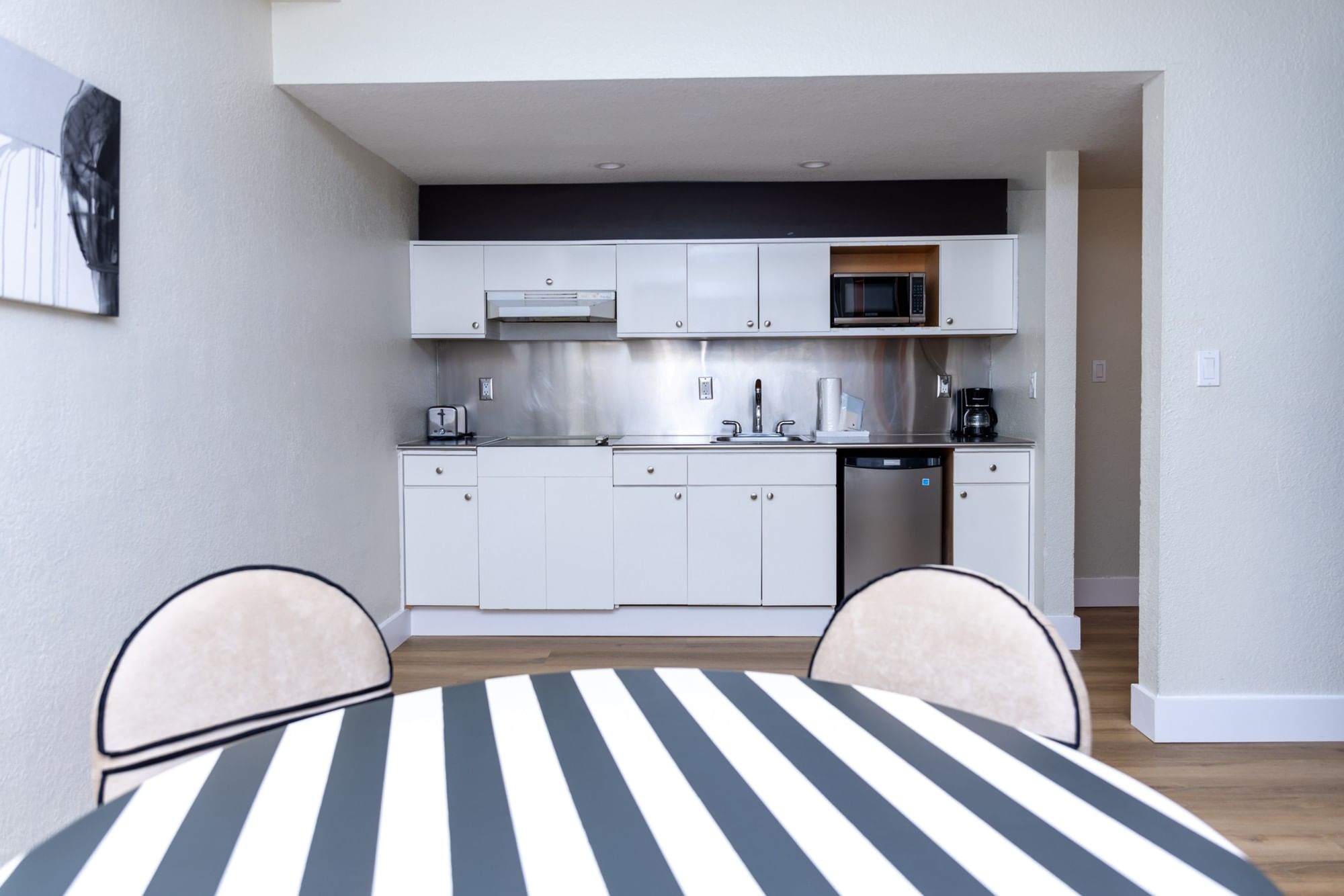 A modern kitchen with white cabinets and stainless steel appliances, including a microwave, toaster, and coffee maker, with a dining table and chairs in the foreground.