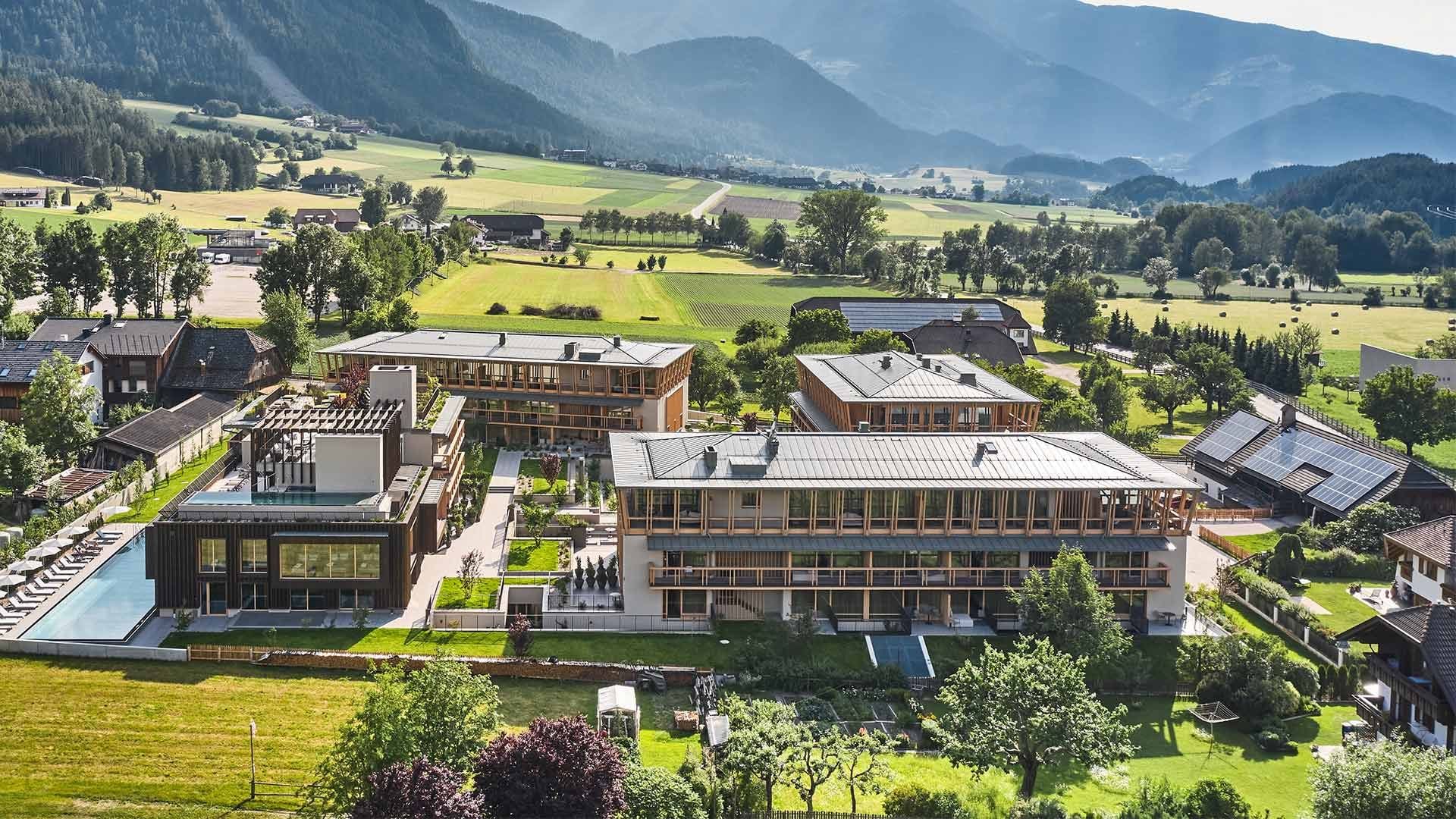 Aerial view of modern hotel complex surrounded by green fields and mountains at Falkensteiner Group