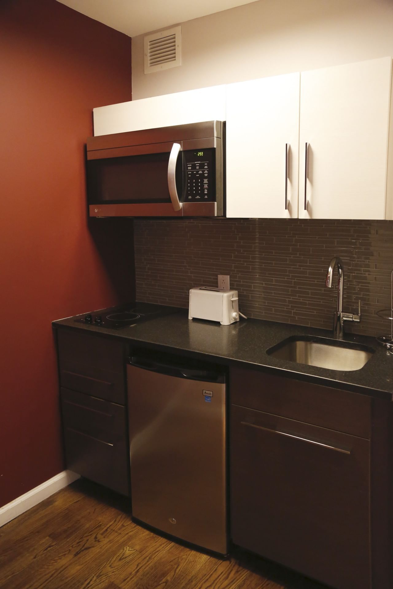 A compact kitchenette with a microwave, mini fridge, sink, and stovetop.