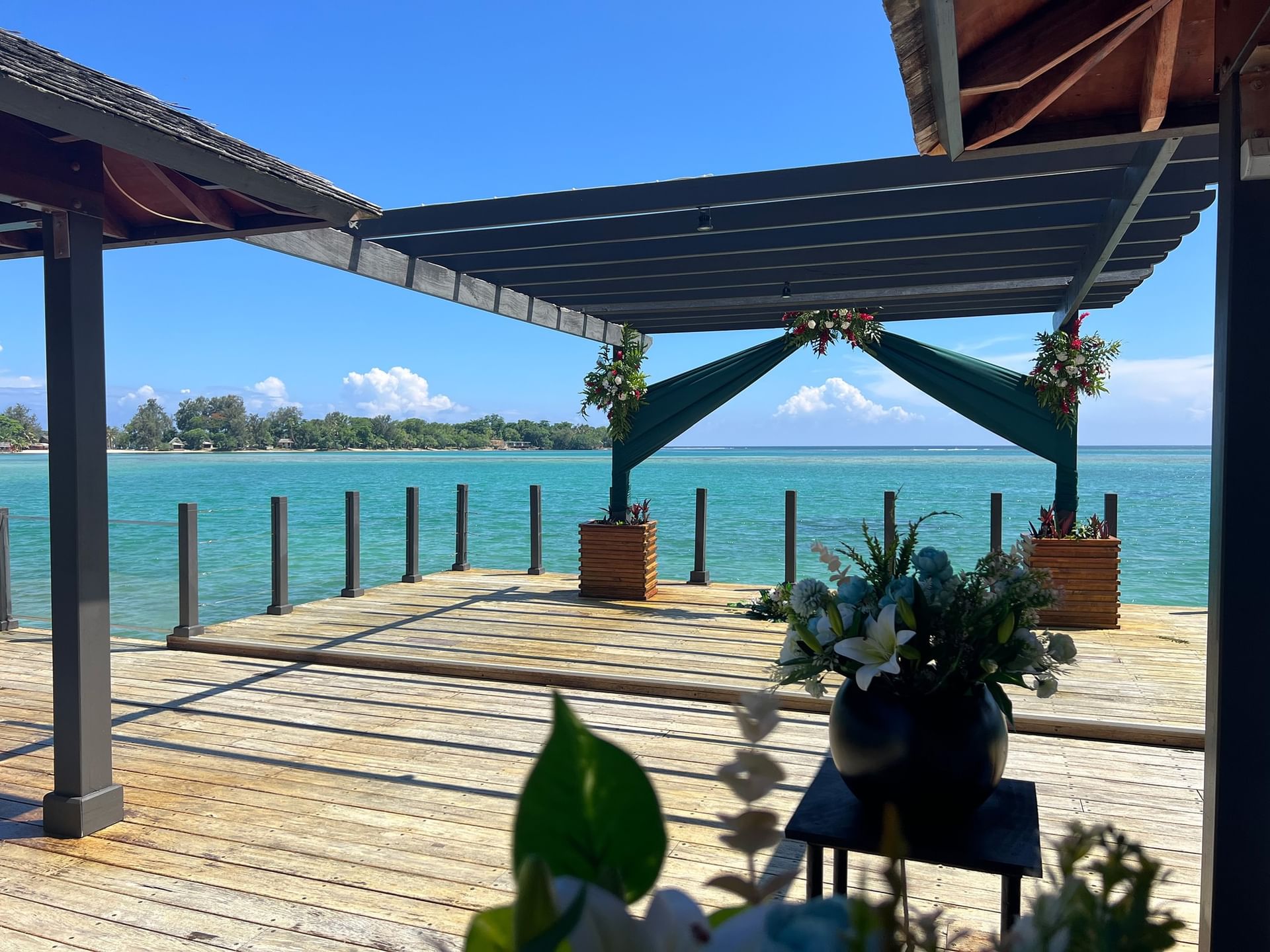 A wooden deck with canopy and flowers overlooking a calm ocean at Warwick Le Lagon - Vanuatu Port Vila