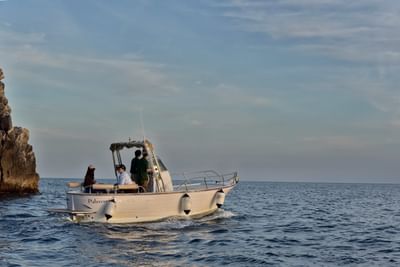 Small motorboat with passengers cruising past rocky cliffs on calm blue waters at Grand Hotel Portovenere