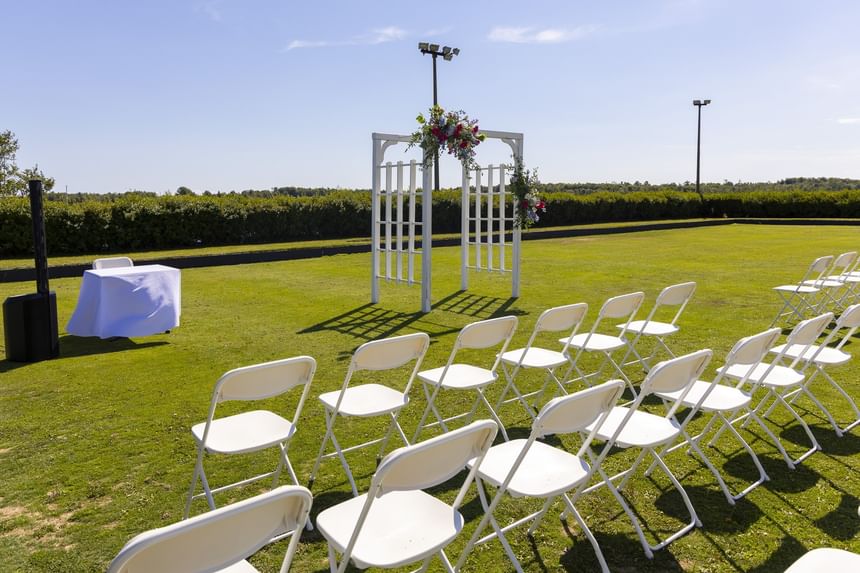 White chairs set up by a wooden wedding arch under a sunny blue sky on the lawn at Rodd Brudenell River Resort