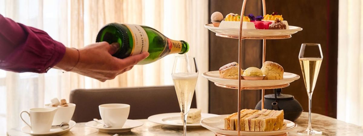 Champagne being poured beside a three-tiered stand with sandwiches, scones, and pastries for Afternoon Tea Indulgence