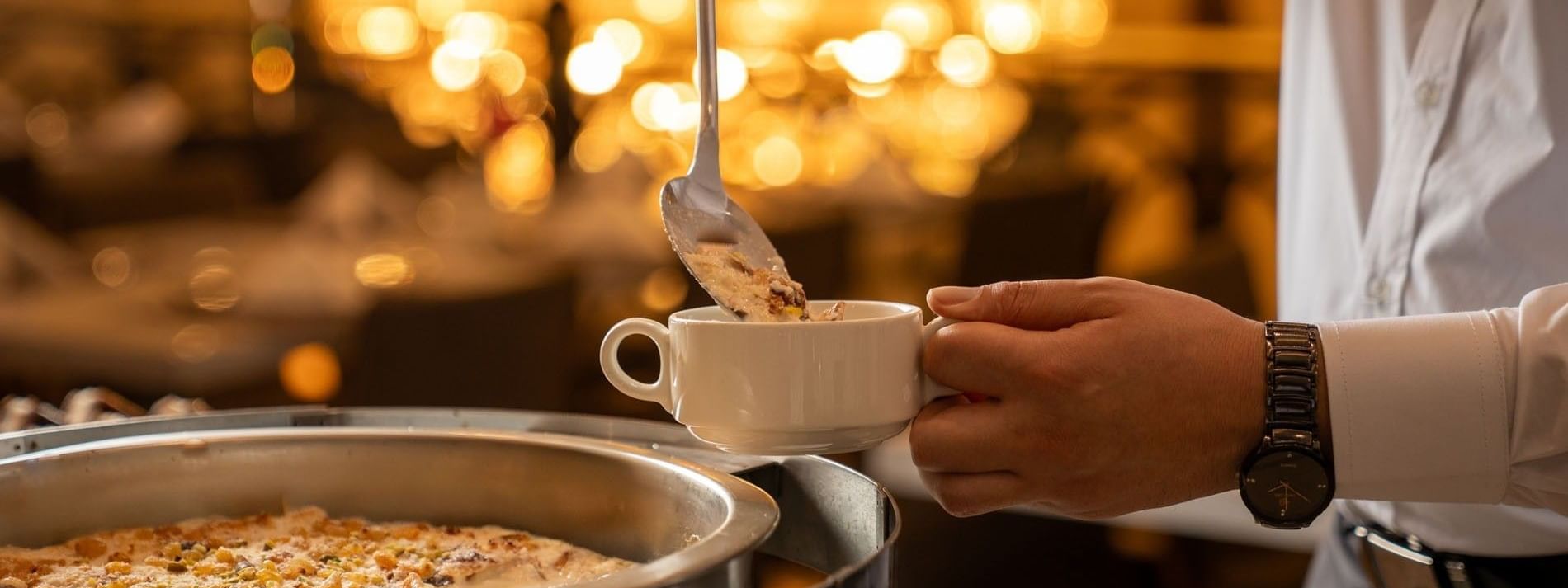 Person ladles dessert topped with nuts into white cup in Al Firdous Restaurant at Saja Warwick Madinah