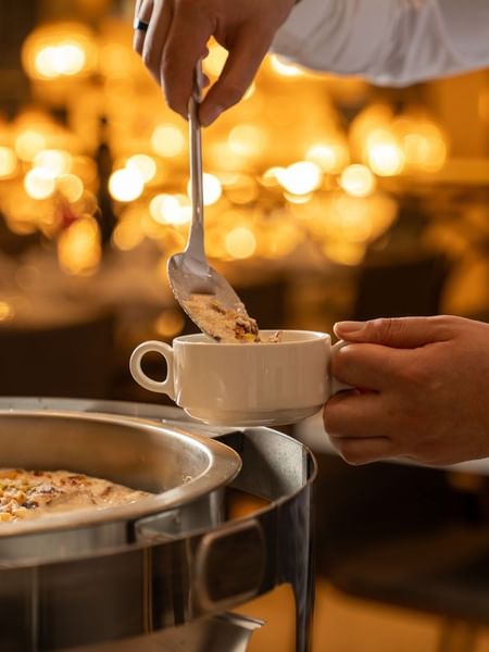 Person ladles dessert topped with nuts into white cup in Al Firdous Restaurant at Saja Warwick Madinah