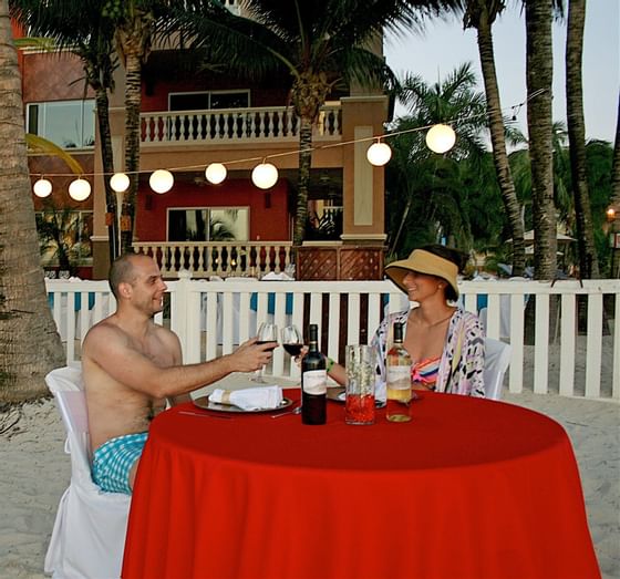 Couple at a table on the beach toasting wine at Infinity Bay