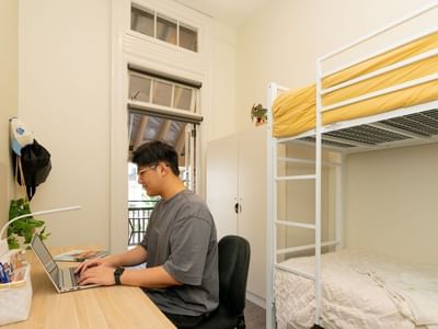 Student working on laptop in Bunk Room Twin Share with Balcony at UniLodge Herston.