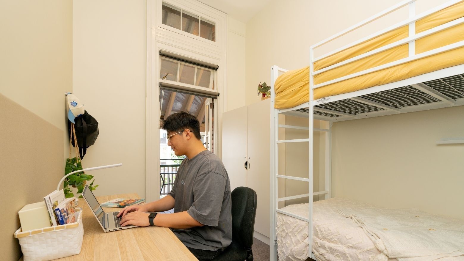 Student working on laptop in Bunk Room Twin Share with Balcony at UniLodge Herston.
