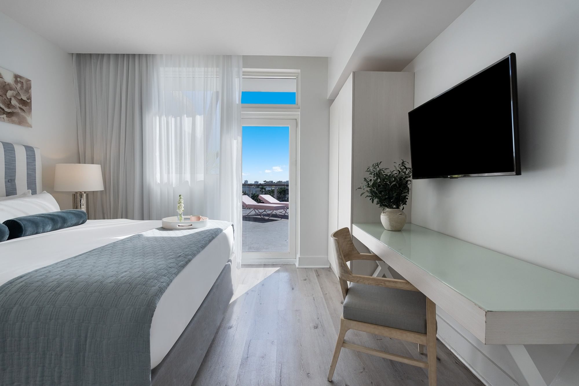 A clean and modern hotel room with a bed, desk, TV, and balcony