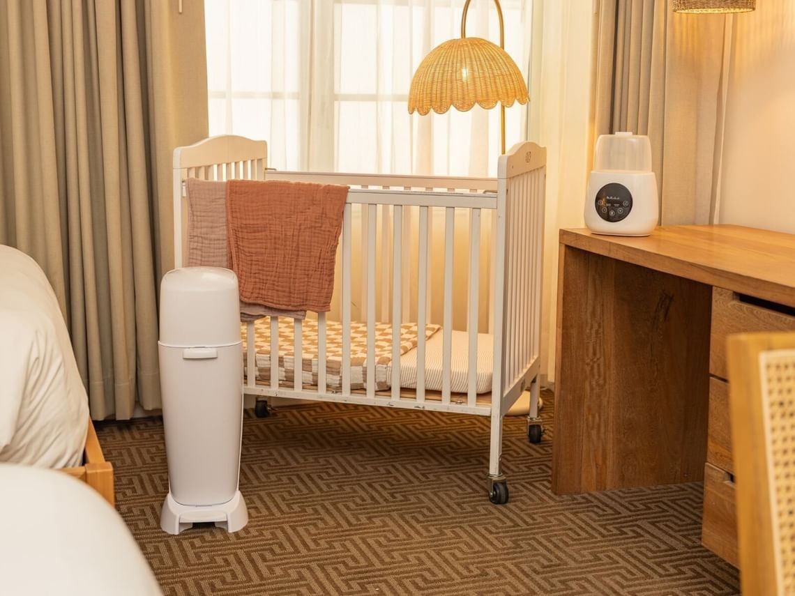 A hotel room with a crib, desk, and bed.