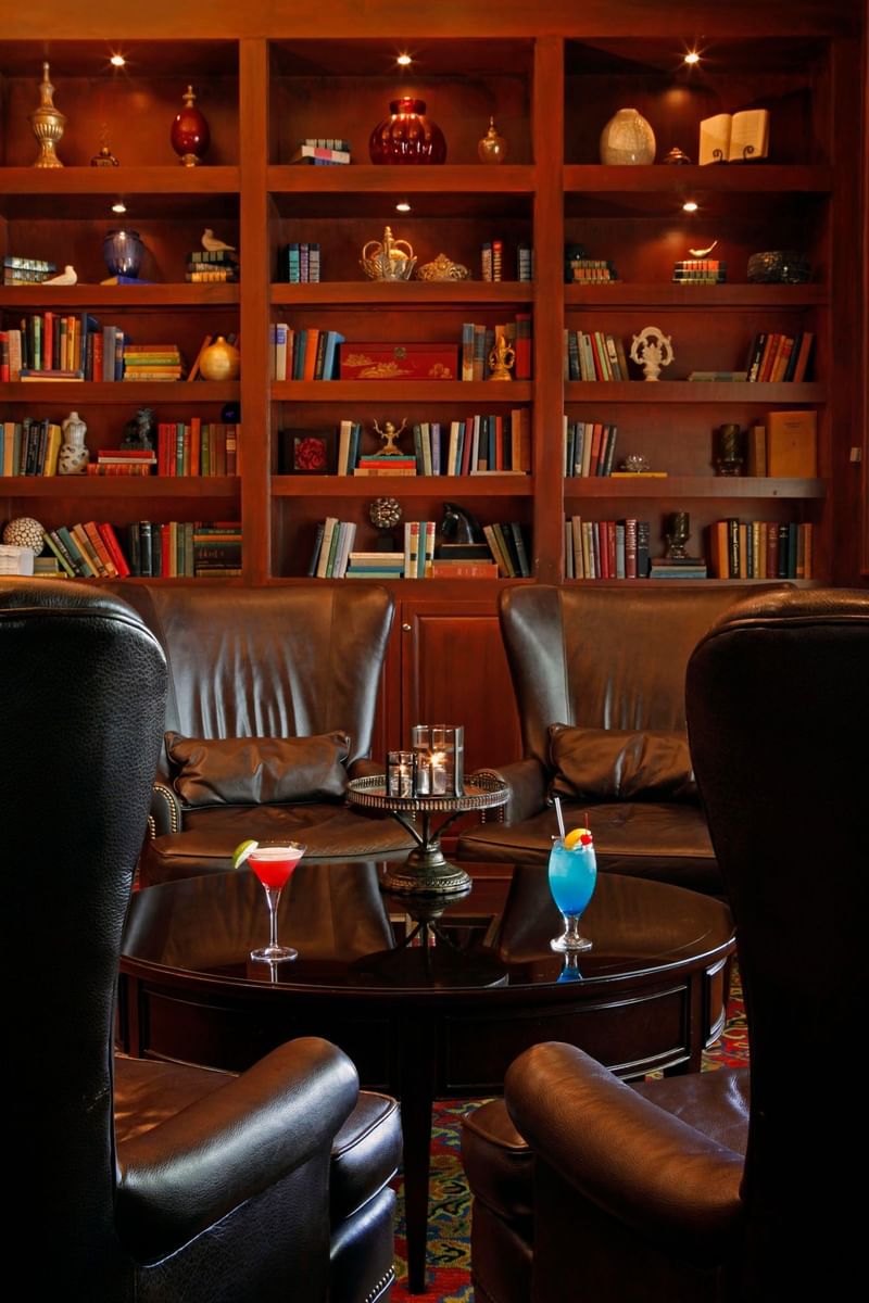 Cocktails on a dark table by leather wingback chairs in a library lounge at Warwick Melrose Dallas