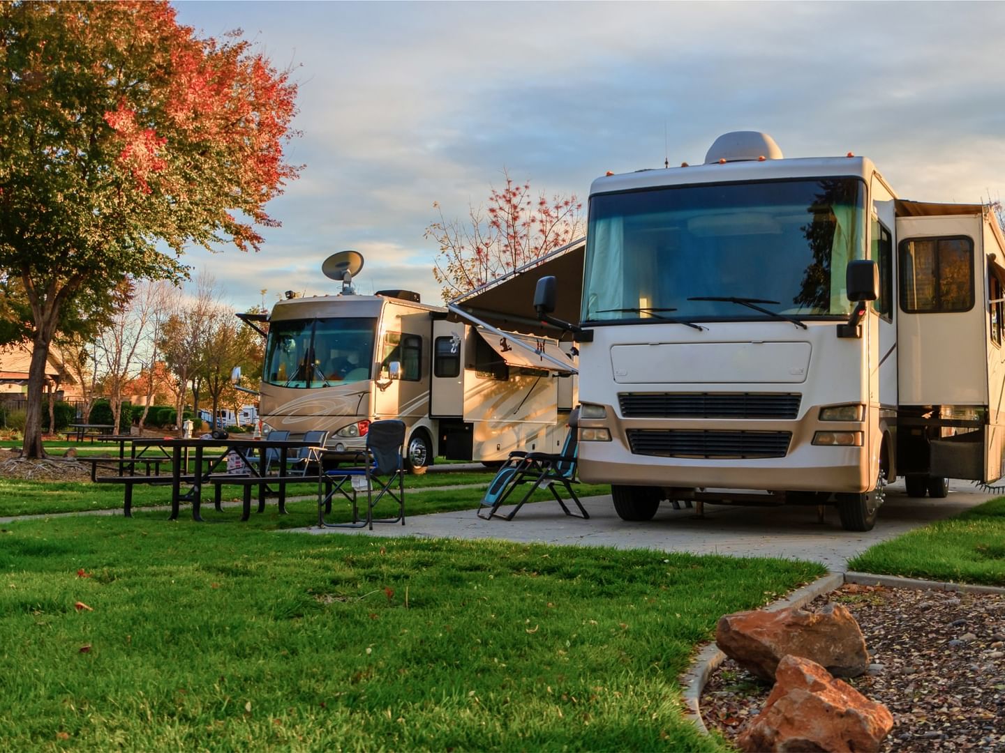 Motorhomes are parked on a grassy area with trees displaying autumn colors in background at Fall Creek Marina & Campground
