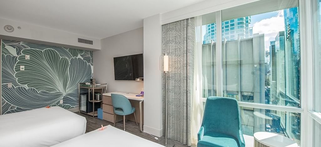 Bright, modern room featuring a bed, teal chair, wall-mounted television, and floor-to-ceiling windows