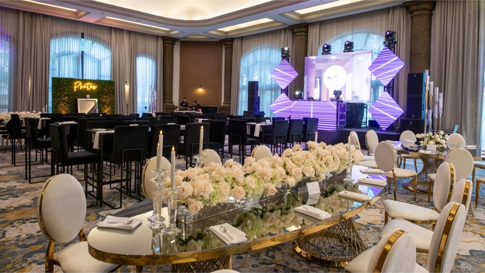 Banquet hall with dining tables, white chairs, floral centerpieces, and stage at Quinta Real Monterrey.