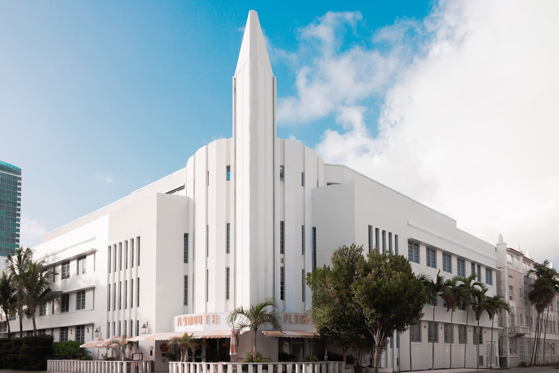 A wide white building with a pointed tower and palm trees in front