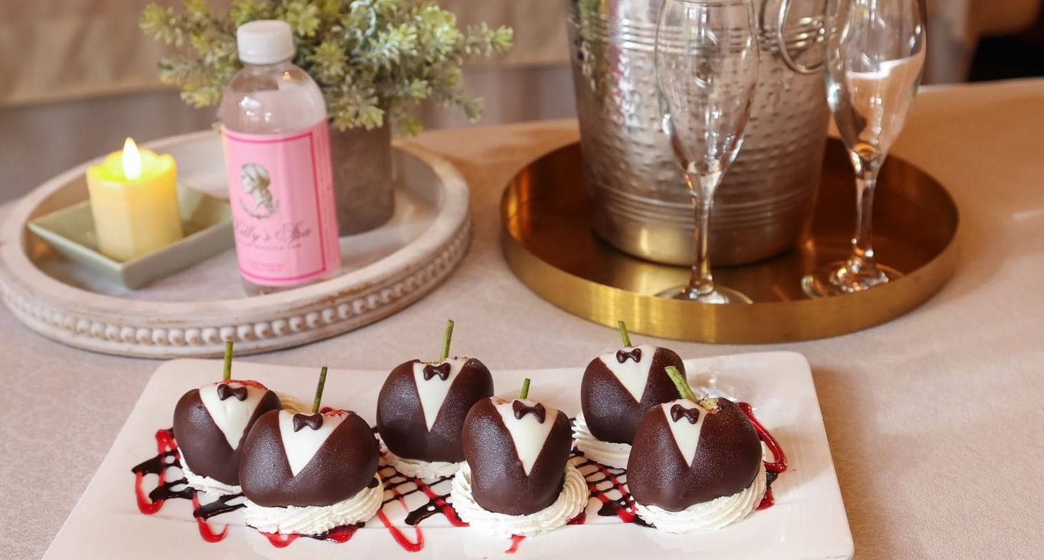 Tuxedo-decorated chocolate strawberries on a plate next to champagne for a romantic spa celebration at Kelly's Spa