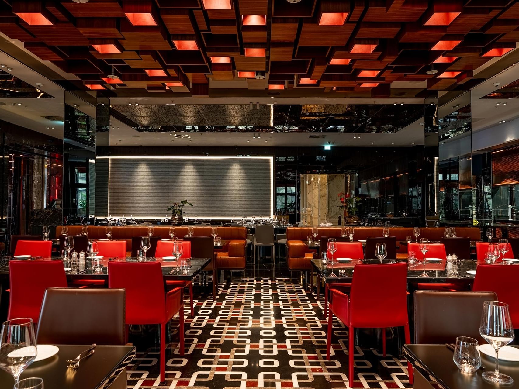 Modern restaurant interior with red and brown seating, geometric patterned flooring, and illuminated ceiling at Titanic Gendarmenmarkt Berlin