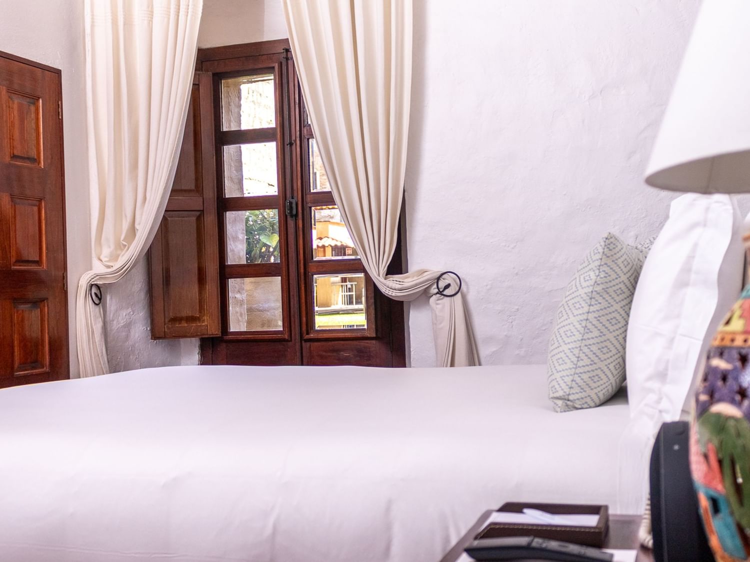 Habitación Novicia Queen con cama grande, ventana y lámpara artesanal en Quinta Real Oaxaca en Oaxaca de Juárez