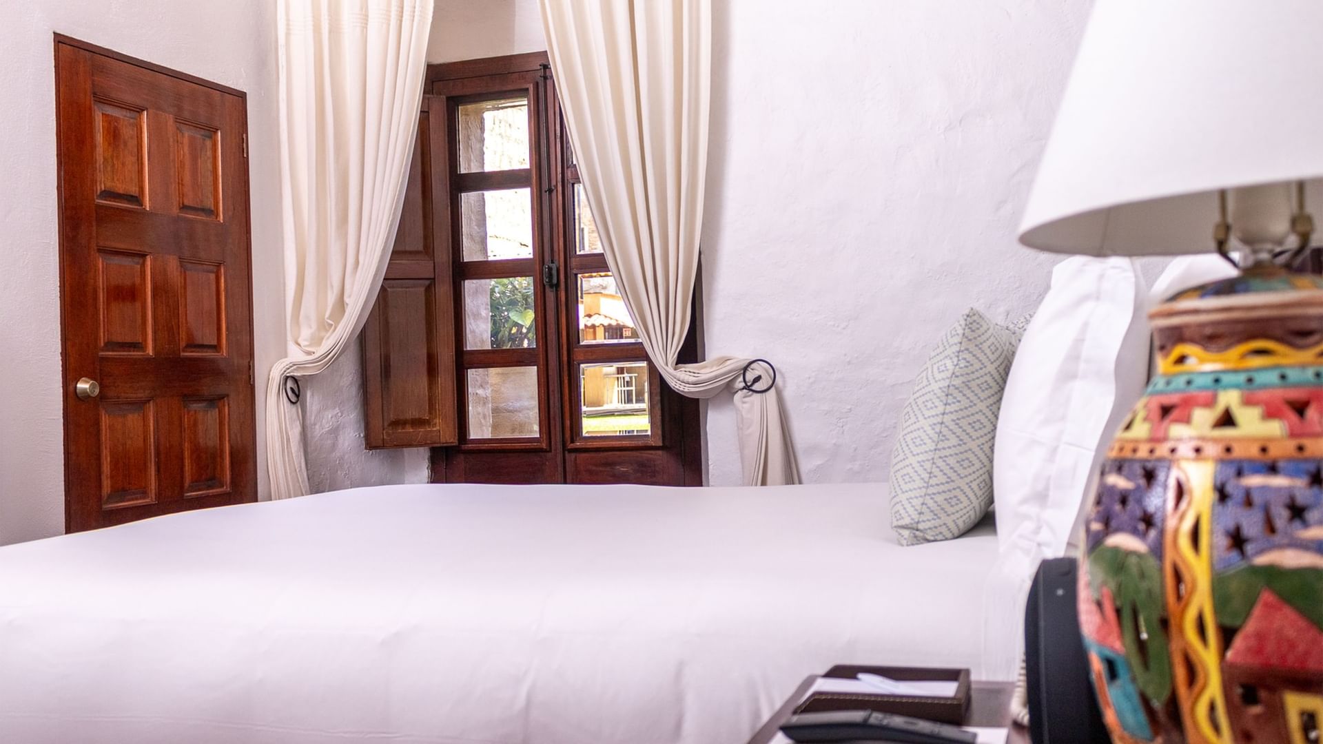 Cozy Queen Novicia room with wooden door and vibrant lamp at Quinta Real Oaxaca.