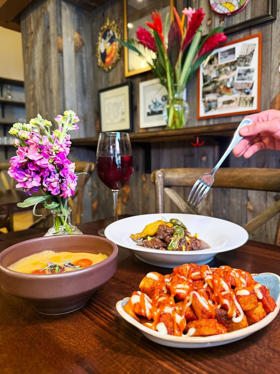 Beef stew by a bowl of soup and spicy potatoes near a wine glass in BOTA at Warwick San Francisco