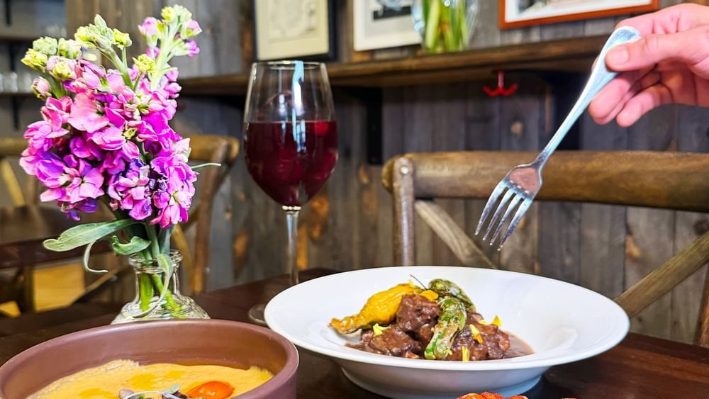Beef stew by a bowl of soup and spicy potatoes near a wine glass in BOTA at Warwick San Francisco