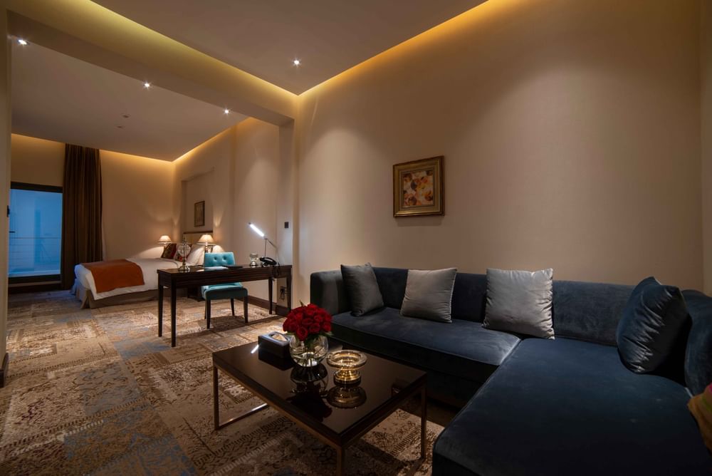 Dark blue sectional sofa by a wooden desk & workspace under warm lighting in Superior King Room at Warwick Al Khobar