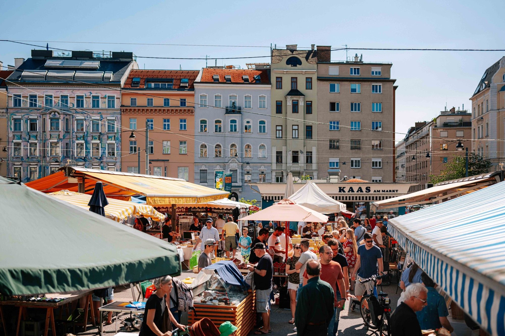 Karmelitermarkt in Vienna with lively market stalls, visitors, sun umbrellas and historic residential buildings