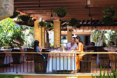 Group of three people dining at an outdoor restaurant with tropical decor and hanging plants.