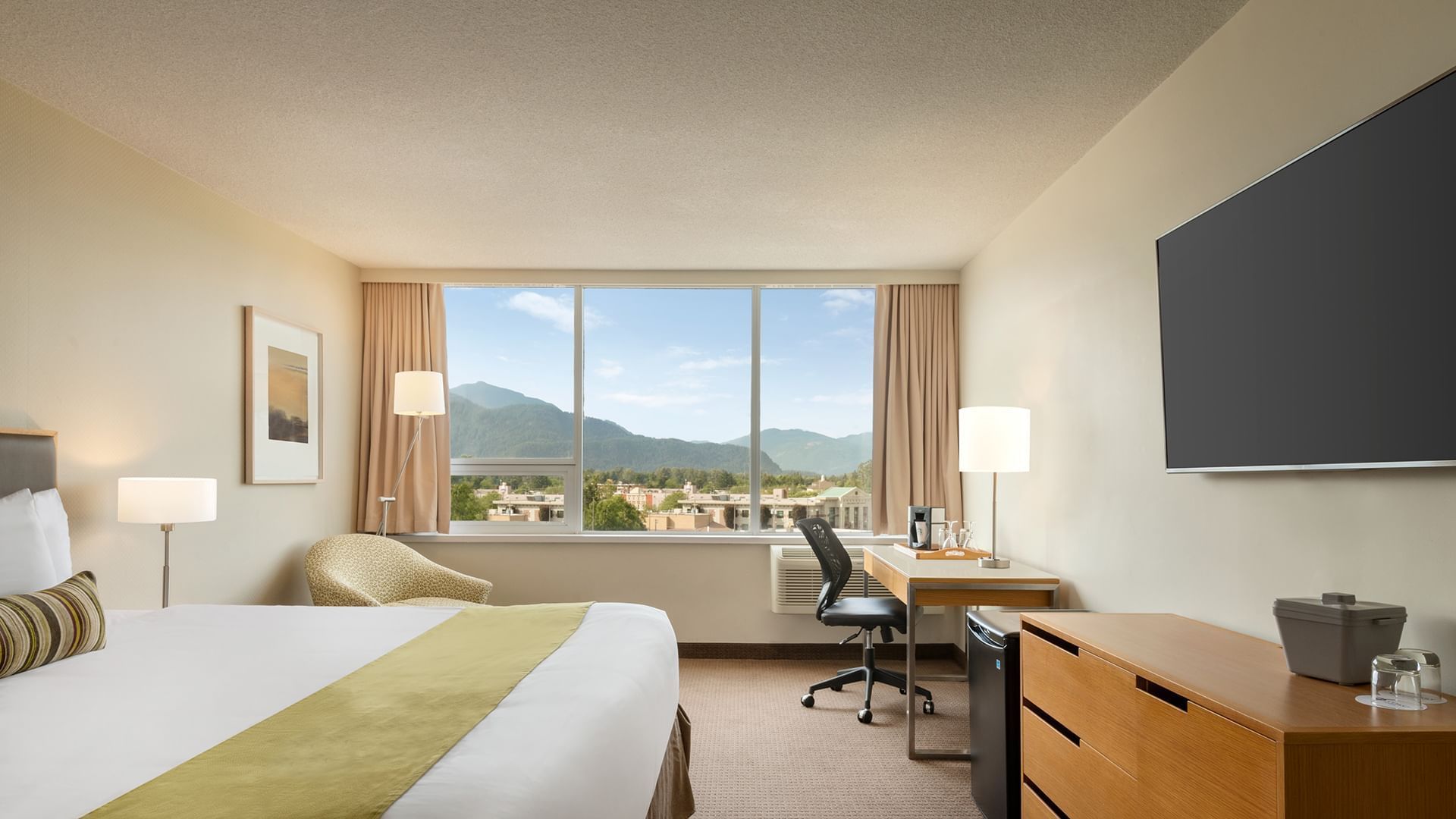 Bed facing TV with desk in hotel room with mountain views