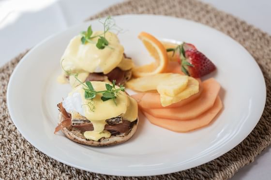 a plate of eggs benedict and sliced fruit
