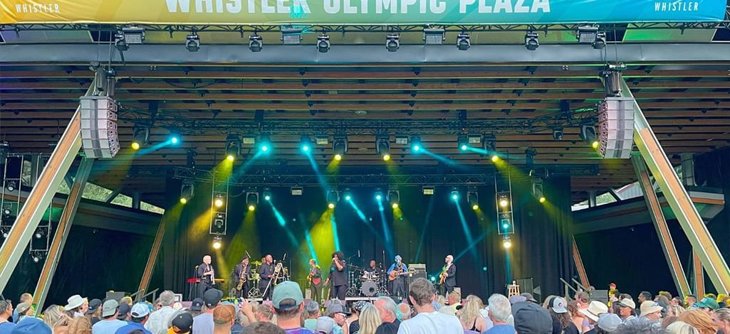Crowd enjoying a live outdoor concert under the banner of Whistler Olympic Plaza during the summer series.
