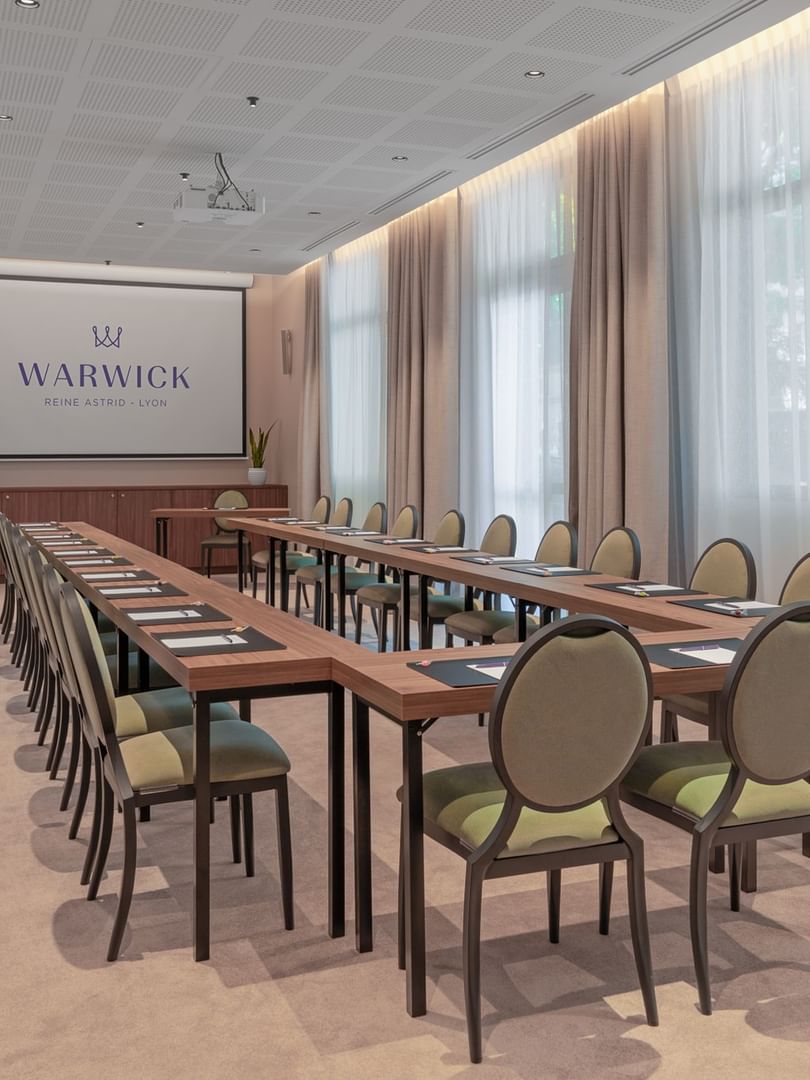 U-shaped table with green cushioned chairs and a projector screen in the Windsor meeting room at Warwick Reine Astrid - Lyon