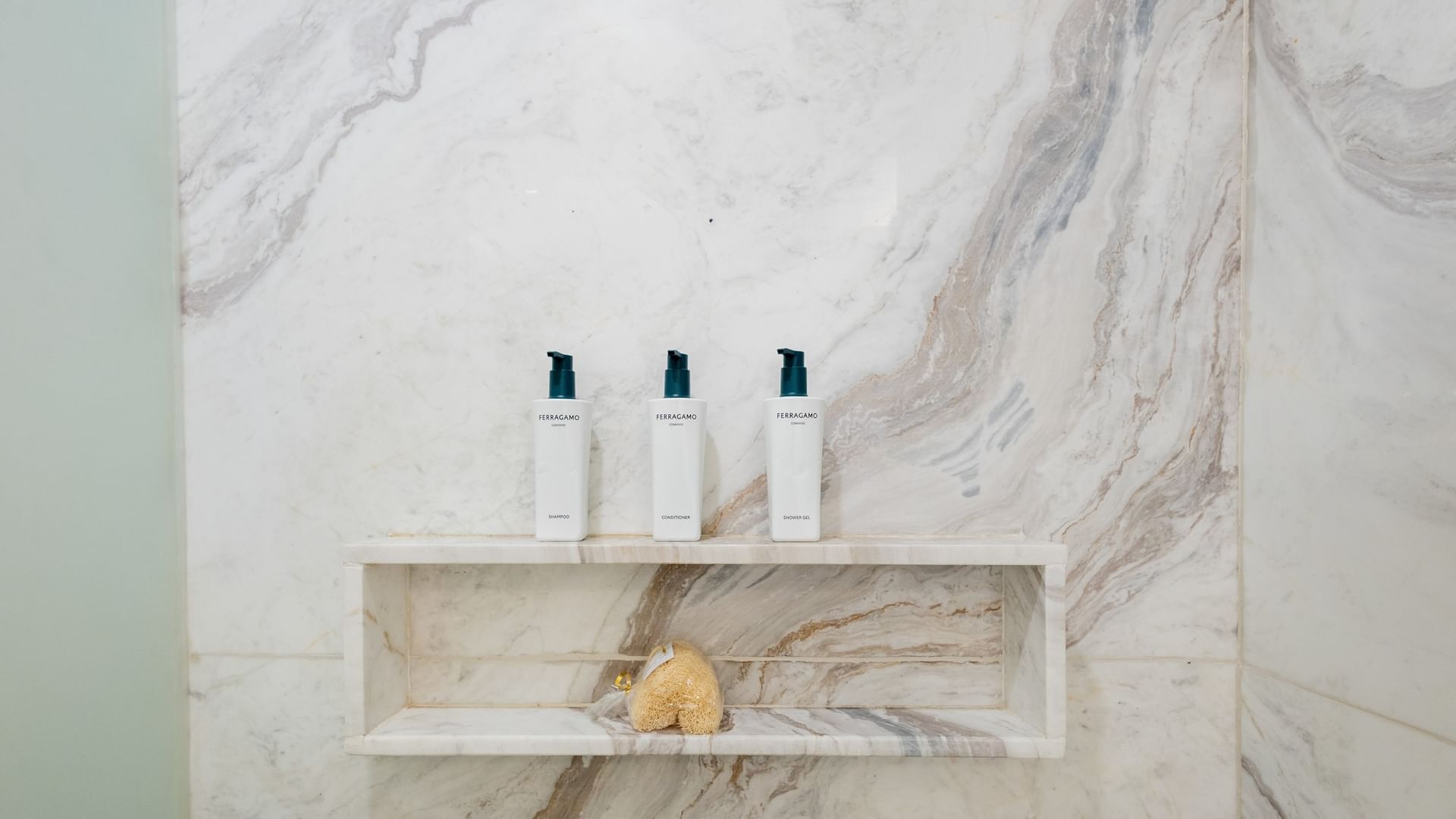 Marble bathroom niche with three white toiletry bottles and a natural sponge at Quinta Real Monterrey
