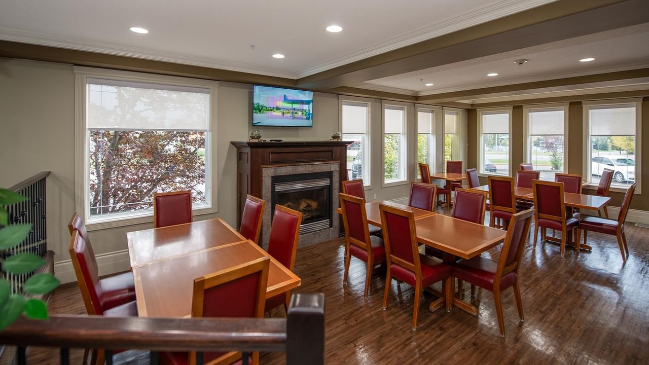 Bright dining area with wooden tables, red leather chairs, fireplace, and large windows at Coast Edson Hotel.