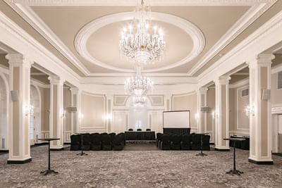 Rows of black conference chairs by a projector screen under large crystal chandeliers at Rodd Charlottetown Hotel