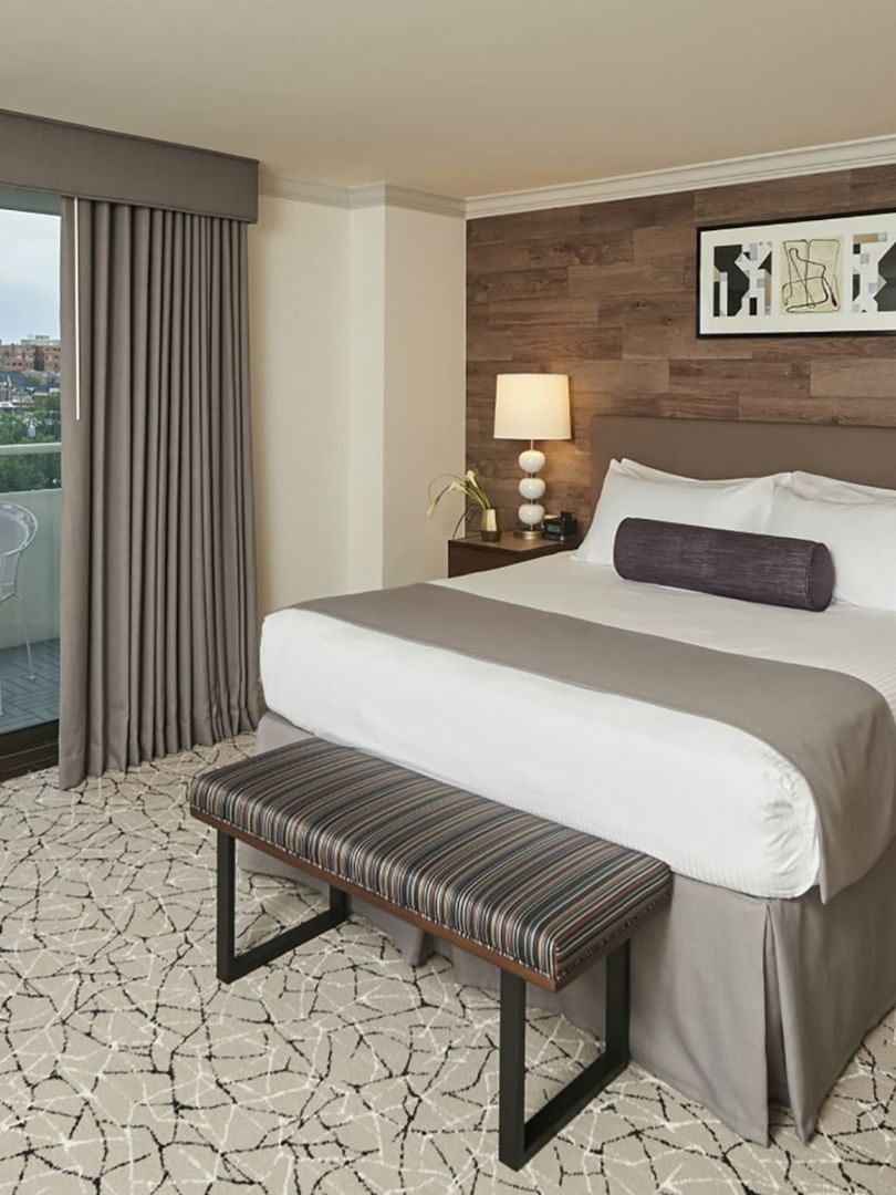 King bed by a striped bench under framed art near a balcony with city views in Deluxe Rooms at Warwick Denver