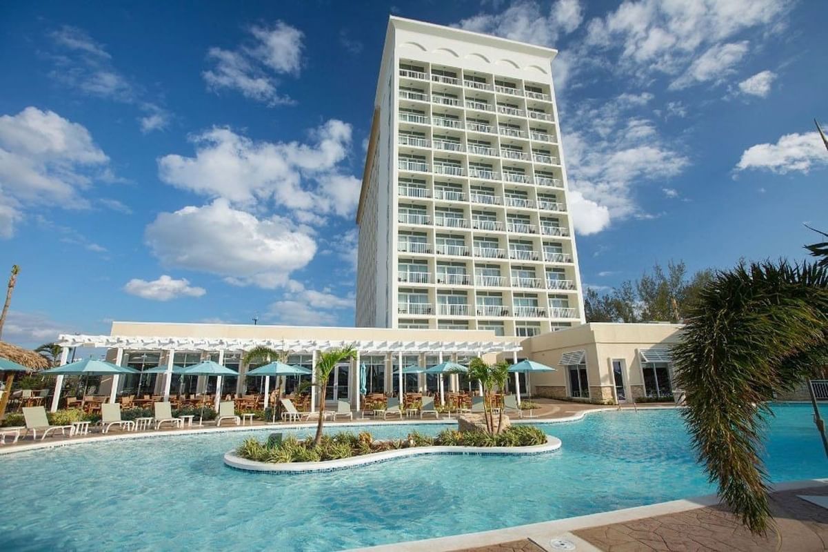 High-rise resort by a turquoise pool with blue umbrellas surrounding a tropical island at Warwick Paradise Island Bahamas