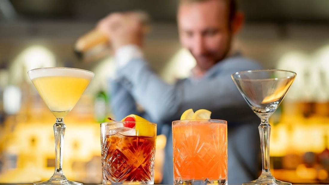 Close-up of cocktails and an empty glass with a blurred bartender at The Marke Bar, Novotel Sydney International Airport