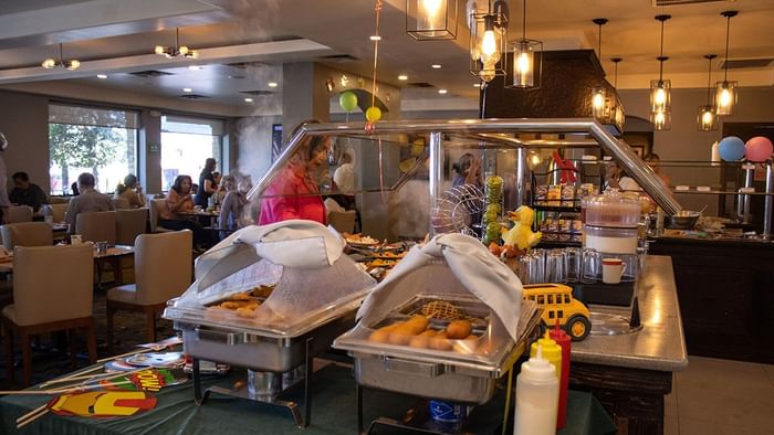 Chafing dishes with corn dogs and waffles at a buffet with a small toy school bus in Palmira Cafeteria at Araiza Calafia