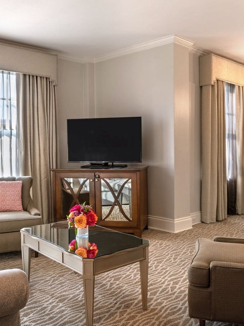 Living area with a TV on a wood cabinet by armchairs under a crystal chandelier in Deluxe Suite at Warwick Melrose Dallas
