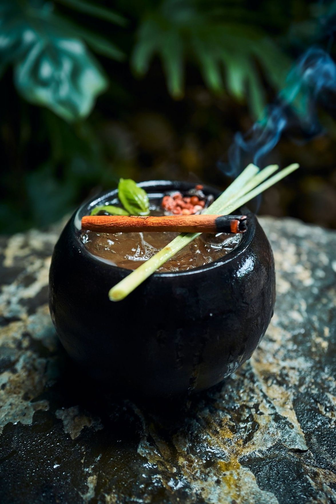 Exotic smoked cocktail served in a dark clay cup with fresh lemongrass and herbs at Cala Luna Boutique Hotel