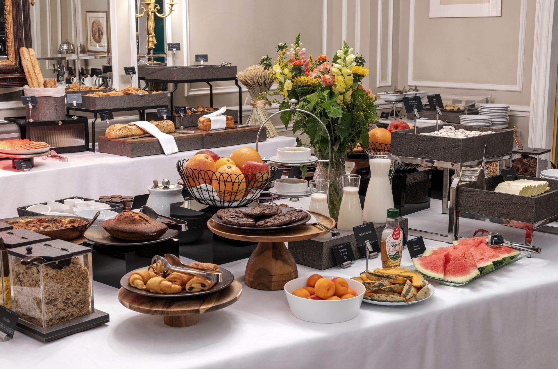 Breakfast buffet spread of fruits and pastries on white tables by floral arrangements at Hotel Westminster Paris
