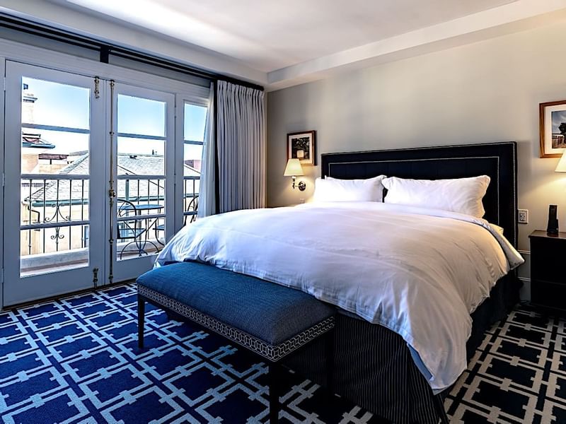 Inviting guest room at El Prado Hotel, with a bed, bench, and French doors leading to a balcony