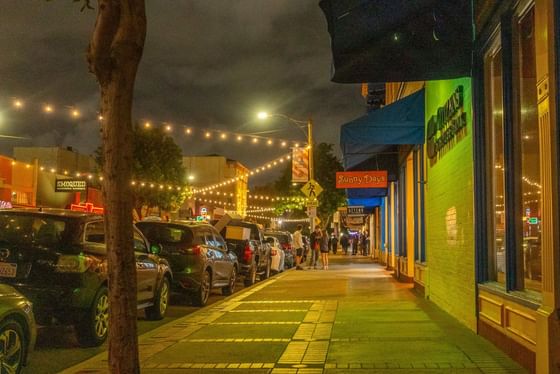 Sidewalk by cars parked on a city street under string lights at night, near Anaheim Portofino Inn & Suites