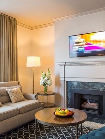 Beige sofa by a round table under a wall-mounted TV near a marble fireplace in Balcony Suite at Warwick San Francisco